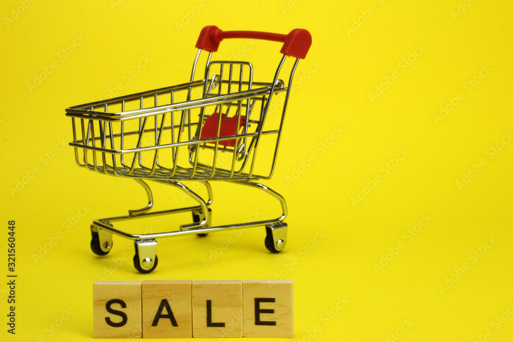 Mini supermarket cart, trolley on a yellow background. Purchases. The Word Sale Mini supermarket cart, trolley on a yellow background. Purchases. The Word Sale