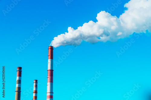 Smoking pipes of the plant against the blue sky, white smoke from the pipes