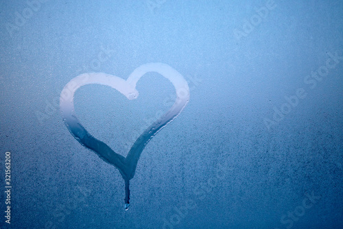 Hand drew heart on glass with drops of condensed steam with drops of water. Hot water vapor condenses on the cold glass in the bathroom. Close up detail of moisture condensation problems