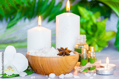 Small glass bottles with aromatic massage oils, wooden bowl of salt, burning candles, green plants are on table. Ayurveda salon concept. Preparation for spa and relax healing treatments.