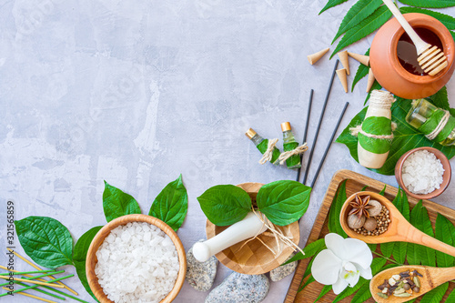 Top view of set for relaxing thai spa treatments. Wooden mortar pounder with herbs, bowl with salt, essential oils, pot with honey, spices, aroma sticks are on cement background. Ayurveda salon.