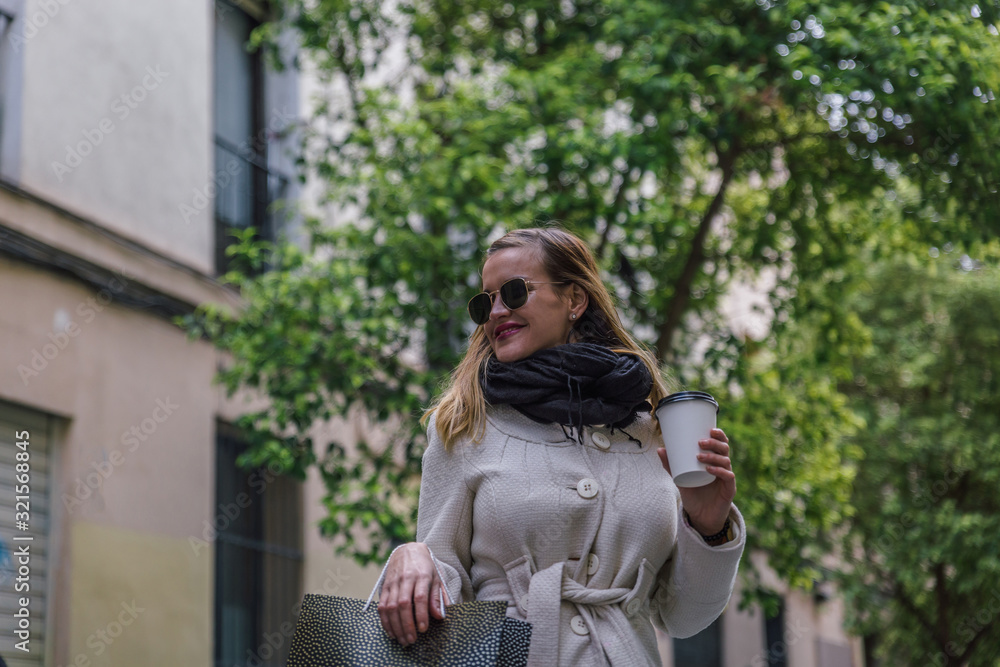Beautiful caucasian blonde woman smiles while having coffee in the street after shopping