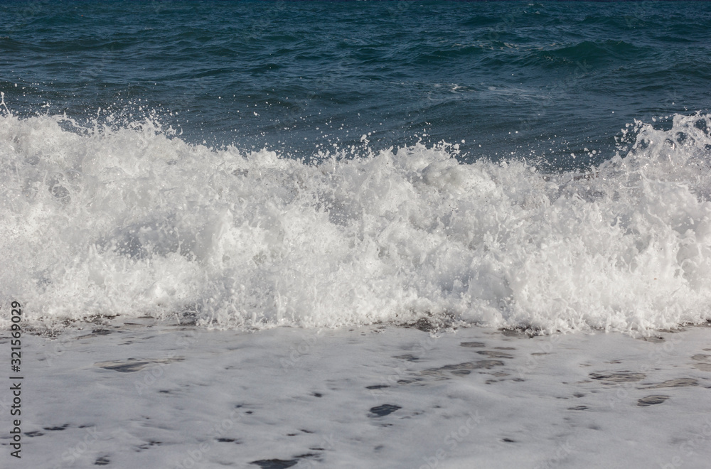 beaches with black volcanic sand and soft volcanic pebbles, with waves of white sea foam on the island of Santorini in Greece