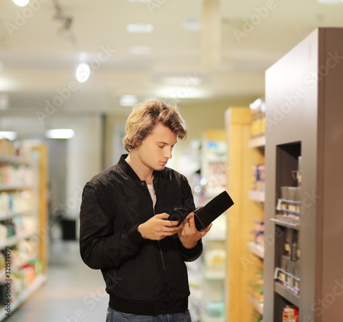 Young man shopping in supermarket, reading product information	