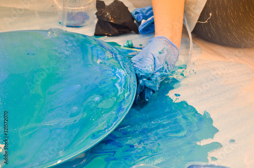 A man in a blue glove beautifully paints draws an acrylic blue multi-colored resin a round home-made board