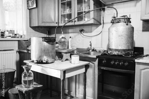 Old-fashioned moonshine machine for creating homemade strong alcohol in the kitchen. Process of distillation, general view. Story about an aged way of distilling moonshine at home. Monochrome effect photo