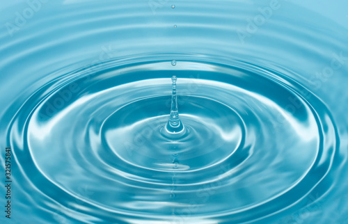 a drop of water falls with a splash into clear, blue water forming circles on the water