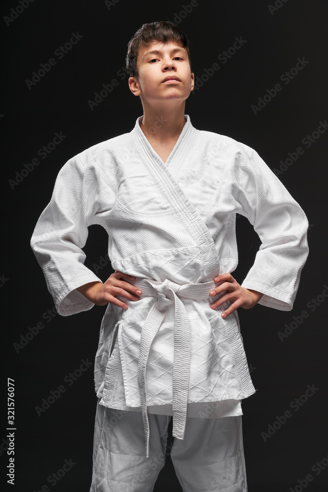 sport concept - a proud teenager dressed in martial arts clothing poses on a dark gray background, studio shoot sport concept - a proud teenager dressed in martial arts clothing poses on a dark gray background, studio shoot