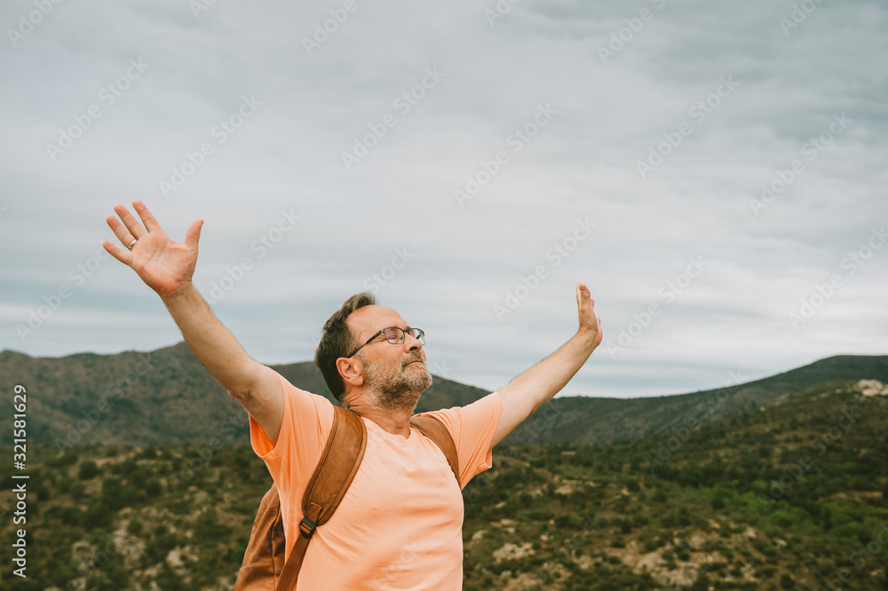 Man standing on the top of the hill, wearing backpack, arms wide open, eyes closed Man standing on the top of the hill, wearing backpack, arms wide open, eyes closed