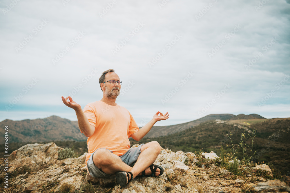 Outdoor portrait of handsome middle age man meditating, relaxing in the top of the mountain Outdoor portrait of handsome middle age man meditating, relaxing in the top of the mountain