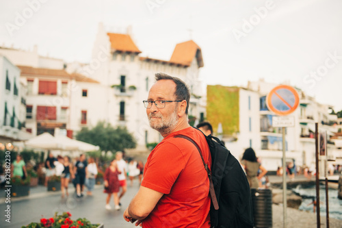 Outdoor portrait of middle age man walking in small europen town, male traveller, wearing back pack, red t-shirt and eyeglasses © annanahabed