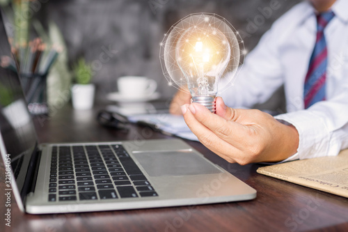 innovation and business creative idea concept, businessman holding light bulb with finance and connection line icon as working in front of laptop on table in office