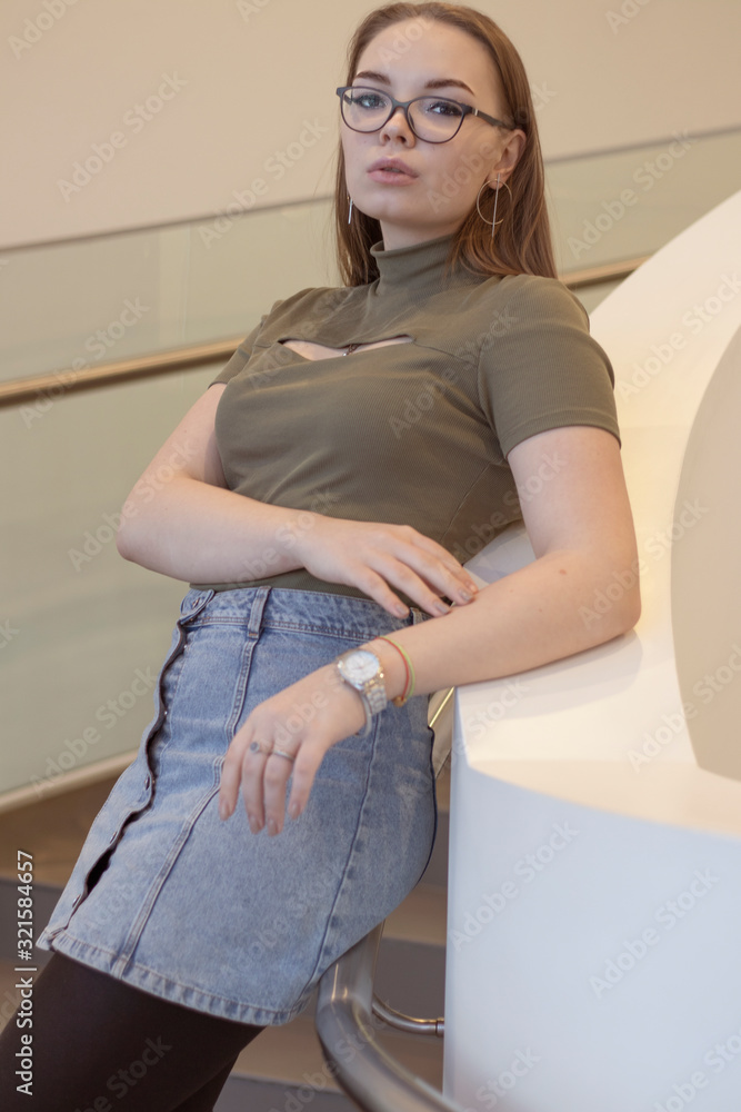 White beautiful girl stands indoors near a transparent railing. White beautiful girl stands indoors near a transparent railing.