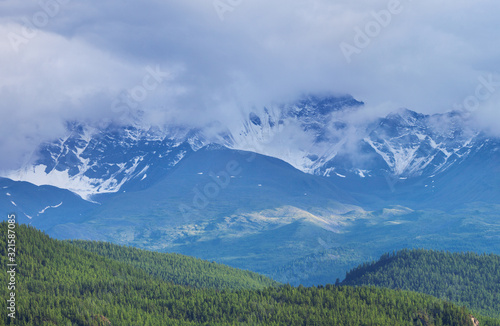 Mountains in the clouds. Snow on the slopes, forest on the hills.