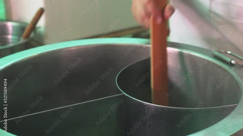 A woman's hand is cooking noodles with hot broth in a stainless steel pot. A woman's hand is cooking noodles with hot broth in a stainless steel pot.