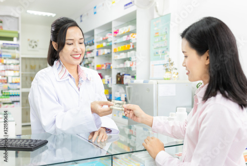 asian female pharmacist receive money from customer, she talk with customer in drugstore, they smile and feeling happy