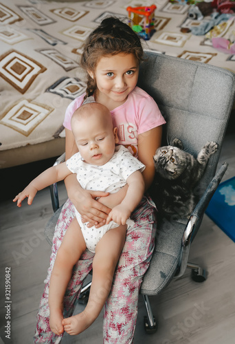 Cute kids boy and girl sit on the chair together with scottish fold kitten.