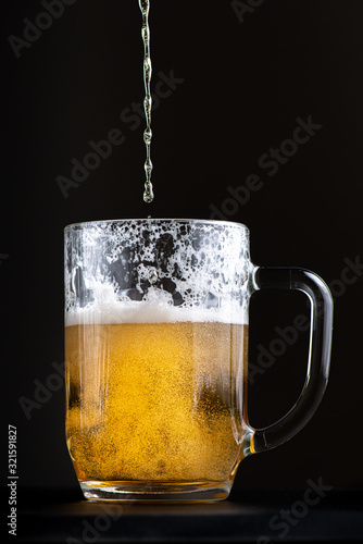 bright and fresh beer is poured into a large glass goblet. Selective focus macro shot with shallow depth of field isolated on black background