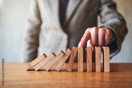 Closeup image of a businesswoman's finger try to stopping falling wooden dominoes blocks for business solution concept
