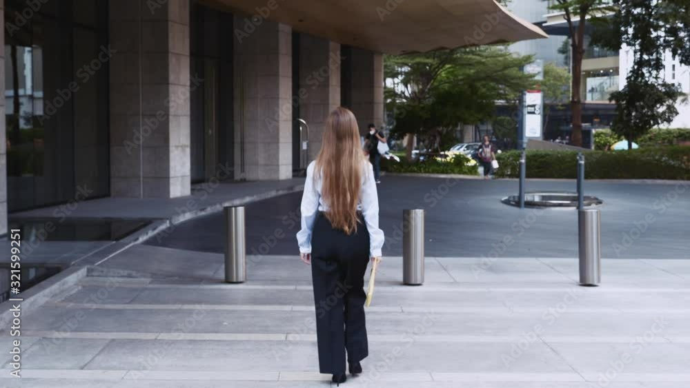 Young Business Woman with Long Hair and Folder with Documents Walking on the Street near Office Building Young Business Woman with Long Hair and Folder with Documents Walking on the Street near Office Building