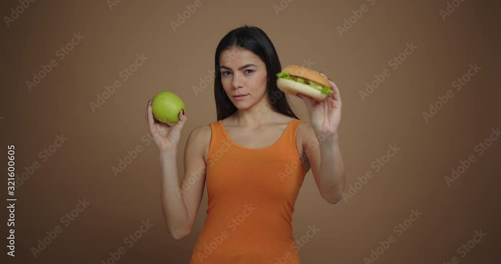 young beautiful woman between apple and burger picks an apple and bites it young beautiful woman between apple and burger picks an apple and bites it