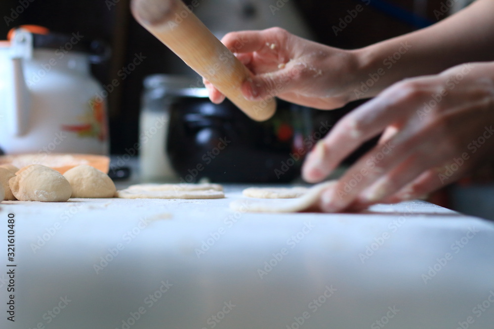 women's hands roll out the dough for dumplings