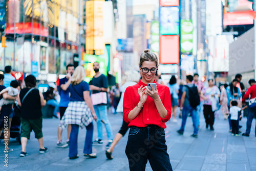 Caucasian female standing in crowded square with mobile phone in hands.Addicted to social network. Millennial technology user. Young woman browsing internet via app on smartphone. Tourist explore city