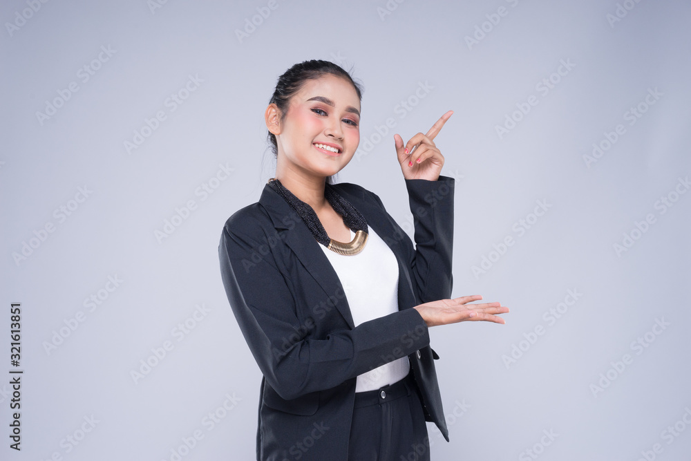 An attractive woman wearing business attire with gestures towards copyspace area isolated on grey. Good for manipulation works for technology, transportation, business or finance theme. An attractive woman wearing business attire with gestures towards copyspace area isolated on grey. Good for manipulation works for technology, transportation, business or finance theme.