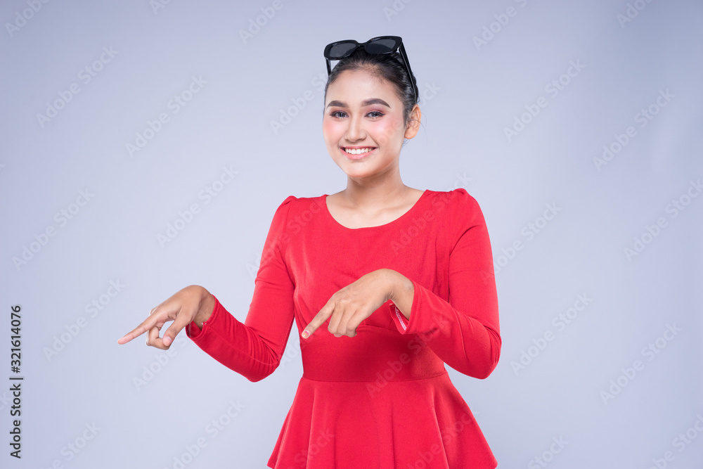An attractive woman wearing casual red attire with gestures and poses towards copyspace isolated on grey. Good for technology, transportation, business or finance concept An attractive woman wearing casual red attire with gestures and poses towards copyspace isolated on grey. Good for technology, transportation, business or finance concept