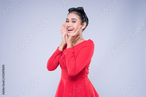 An attractive woman wearing casual red attire with gestures and poses towards copyspace isolated on grey. Good for technology, transportation, business or finance concept