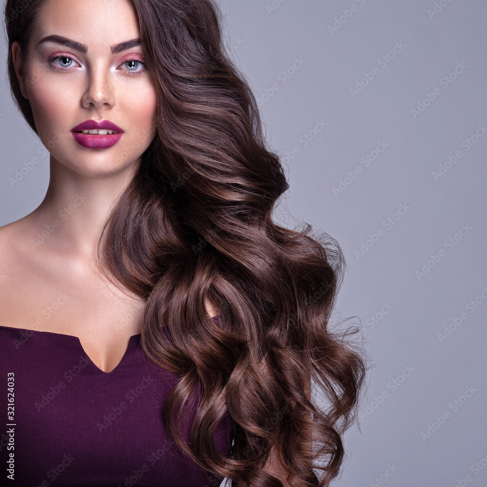 Face of a beautiful woman with long brown curly hair. Fashion model with wavy  hairstyle. Attractive young girl with curly hair posing at studio. Female  face with purple makeup. Violet make-up. Stock