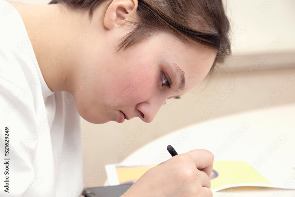 Selective focus. Close-up portrait of teenage girl indoors. She draws with a pencil, passionate about her occupation. Selective focus. Close-up portrait of teenage girl indoors. She draws with a pencil, passionate about her occupation.
