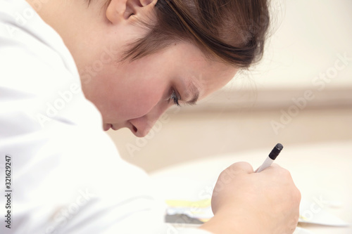 Selective focus. Close-up portrait of teenage girl indoors. She draws with a pencil, passionate about her occupation.