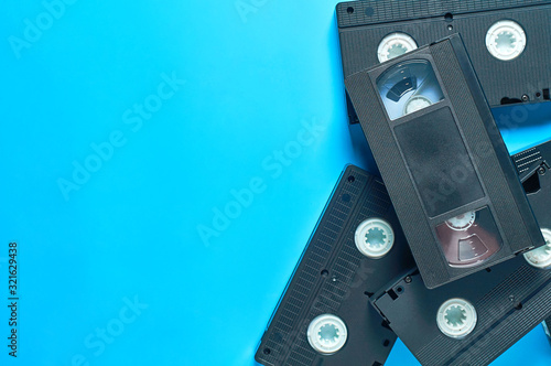 Heap of black old plastic vhs video cassettes lies on blue desk. Concept of 90s. Copy space. Top view