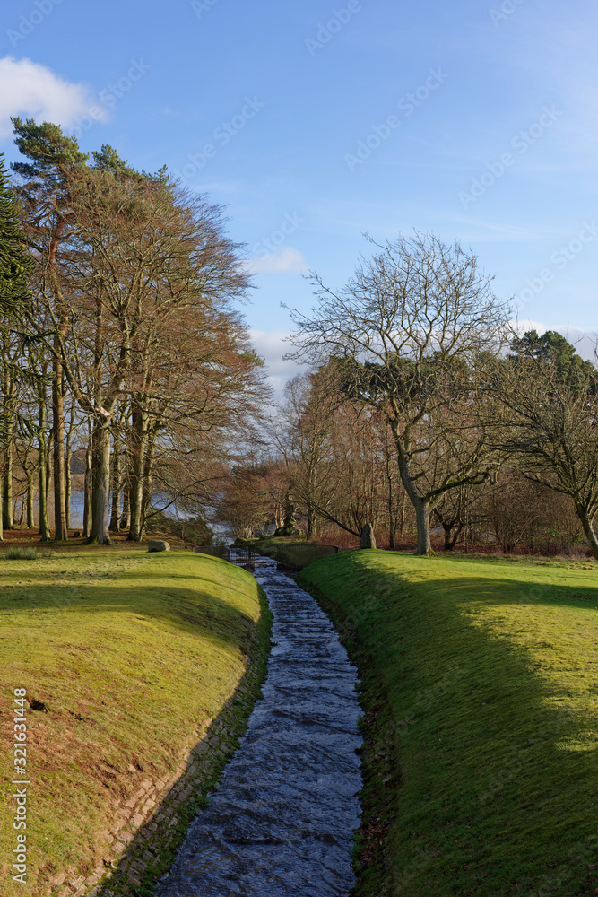 A small man made stream with water flowing into the Reservoir between the trees in a graceful curve on a sunny day in February. A small man made stream with water flowing into the Reservoir between the trees in a graceful curve on a sunny day in February.