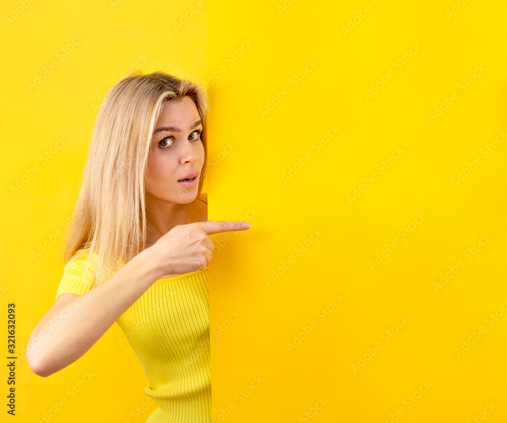 Young woman looking at camera with pointing gesture on a yellow wall. Copy space for banner Young woman looking at camera with pointing gesture on a yellow wall. Copy space for banner