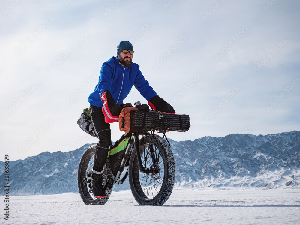 A male traveler rides a fatbike on a frozen mountain lake. Traveling in the winter. Extreme expedition