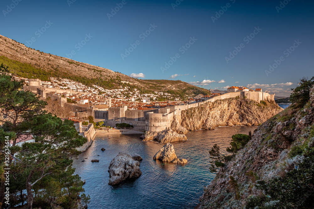 Medieval fort of Old Town of Dubrovnik with round tower inside ancient brick walls, Croatian flag on the top, blue sea with promontories on foreground