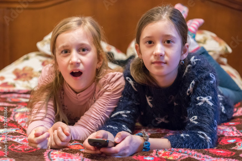 Two happy girls watching tv or movie. A horizontal photo of two young pretty smiling sisters lying on bed and watching their favourite serials