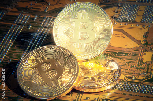 Three big golden physical bitcoins (a digital virtual crypto-currency) over a computer motherboard, with a shiny direct light. photo