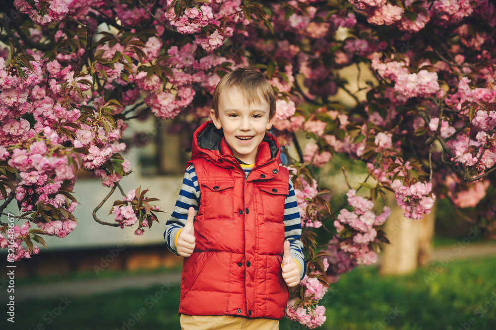 Spring day. Fashionable kid in spring park. Spring pink sakura blossom. Cute little stylish boy in the city. Kids fashion and trendy clothes Spring day. Fashionable kid in spring park. Spring pink sakura blossom. Cute little stylish boy in the city. Kids fashion and trendy clothes