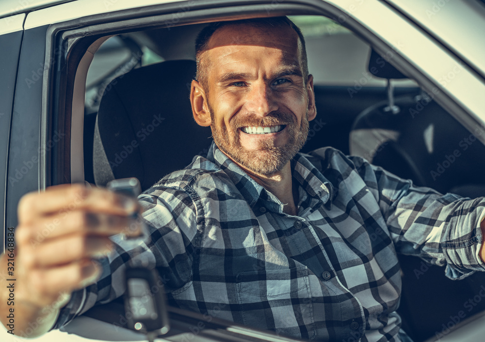 A male driver stands near a white car with a key in his hand and smiles. Toned photo. A male driver stands near a white car with a key in his hand and smiles. Toned photo.