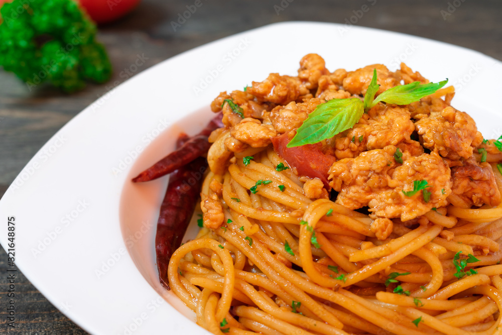 Spicy spaghetti pasta with fried chicken and chili in white dish on black wooden table.