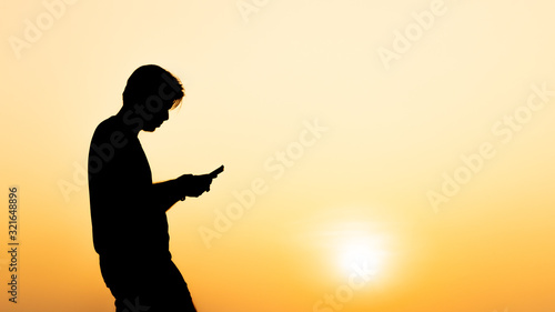 Silhouette young man using smartphone during sunset