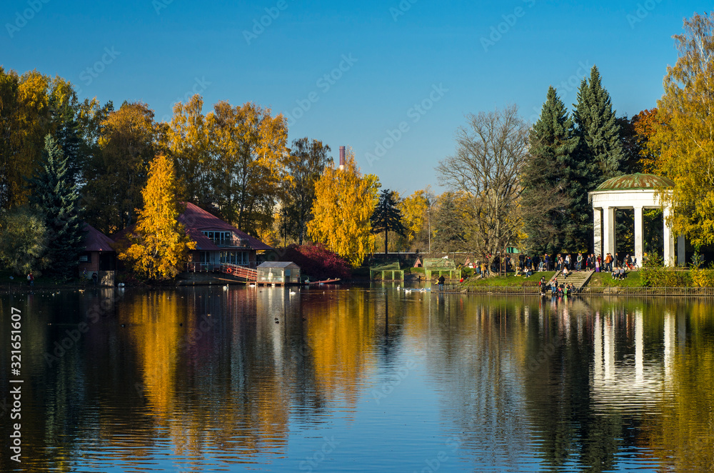 Golden autumn in a beautiful city park. Yellow trees in a mirror reflection of a blue lake. Krestovsky city park. Autumn park with green grass. SPb, Russia, October 17, 2019