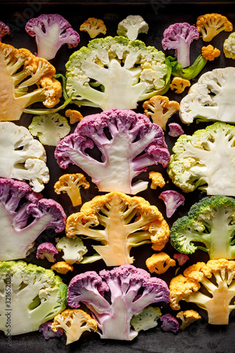 A top view of sliced colorful cauliflowers prepared for baking on a black background. Healthy vegan food © pbd Studio
