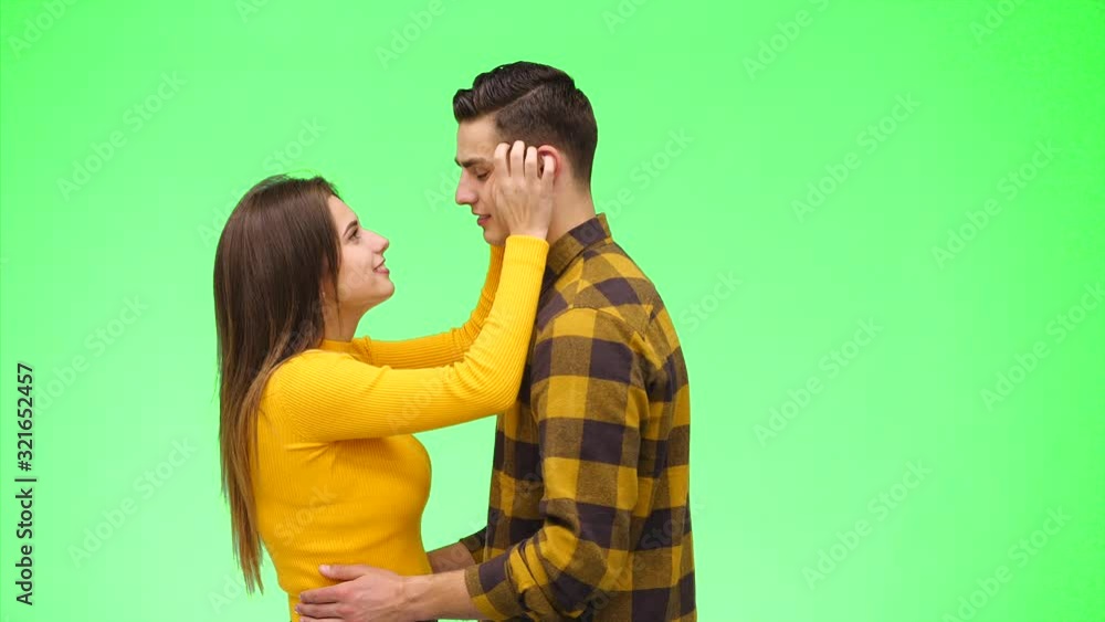 Curious girl is pulling her boyfrind's cheeks and ears on a green background. Close up. Copy space. 4K. Curious girl is pulling her boyfrind's cheeks and ears on a green background. Close up. Copy space. 4K.