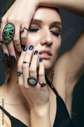 Young woman with eyes closed and many bijouterie rings with stones on fingers
