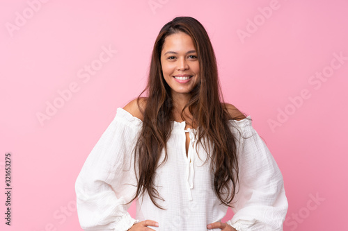 Young Brazilian girl over isolated pink background posing with arms at hip and smiling