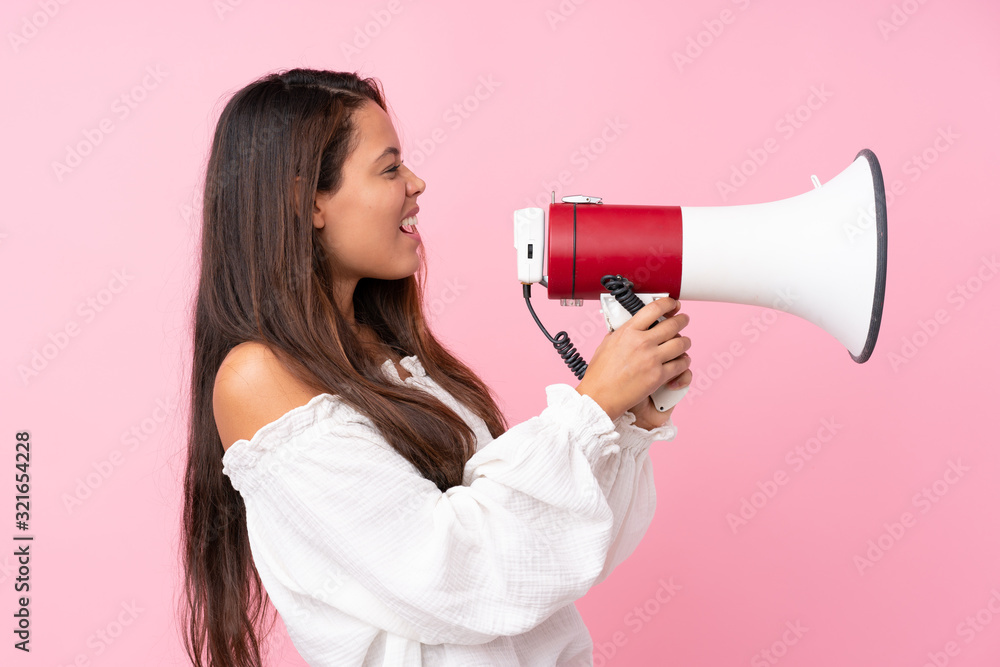 Young Brazilian girl over isolated pink background shouting through a megaphone Young Brazilian girl over isolated pink background shouting through a megaphone